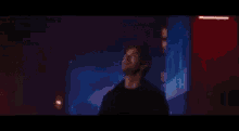 a man in a black jacket is standing in a dark room with a blue light behind him .