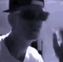 a man wearing a hat and sunglasses is smoking a cigarette in a dark room .