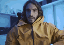 a man with long hair wearing a yellow jacket