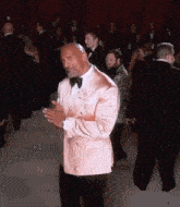 a man in a pink tuxedo and bow tie is clapping
