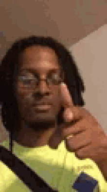 a man with dreadlocks and glasses is giving a thumbs up .