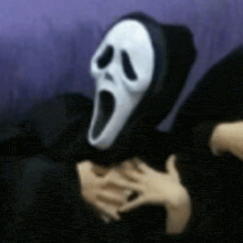 a person wearing a scream mask is laying down on a couch .