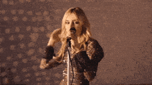 a woman is singing into a microphone with her arms up