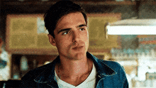 a man wearing a denim jacket and a white shirt is sitting at a table in a bar .