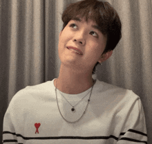 a young man wearing a striped shirt and a necklace with a red heart on it