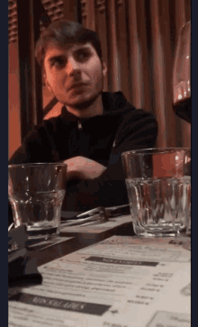 a man sits at a table with glasses of water and a menu