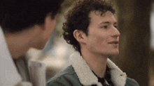 a man with curly hair wearing a green jacket