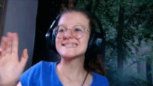 a young woman wearing headphones and glasses is smiling and waving .