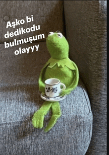 a kermit the frog is sitting on a couch with a cup of coffee