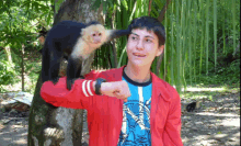 a young man in a red jacket holds a monkey on his arm