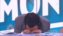 a man in a suit is covering his face with his hands in front of a sign that says mun .