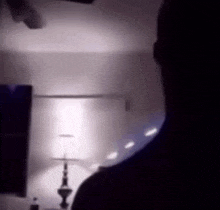a man is standing in a dark room with a lamp in the foreground .