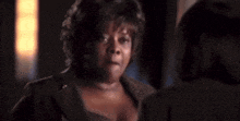 a woman in a suit is talking to another woman in a dark room