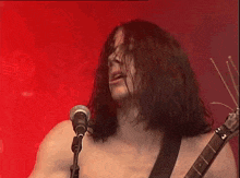 a shirtless man singing into a microphone while holding a guitar