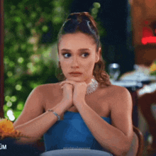 a woman in a blue strapless dress sits at a table with her hands folded
