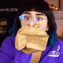a woman wearing glasses is holding a brown paper bag over her mouth ..