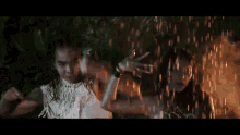 a man and a woman are dancing in the rain in front of a fire and smoke .