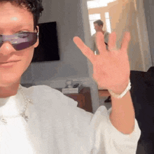 a man wearing sunglasses and a white shirt is waving his hand in a room .