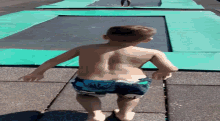 a shirtless boy in hawaiian shorts is standing on a trampoline
