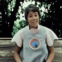 a woman is sitting on a bench wearing a blue vest with a circle on it .