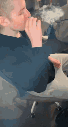 a man in a blue sweater is sitting in a chair smoking a cigarette