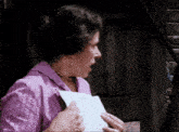 a woman in a purple shirt is holding a piece of paper in her hand