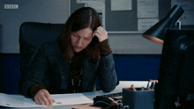 a woman sits at a desk with a bbc logo on the bottom right