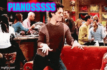 a man is dancing on a red couch in front of a crowd of people with the words pianosss written above him .