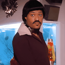 a man with a mustache and a wig is standing in front of a lava lamp