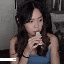 a woman wearing headphones and a blue tank top is drinking from a cup with a $ 500 sticker on the bottom