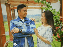 a man in a denim jacket is standing next to a woman in a white dress