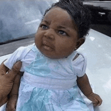 a baby in a blue dress is making a funny face while being held in a person 's hand .