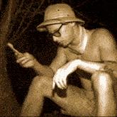 a shirtless man wearing a hat and sunglasses is looking at his cell phone