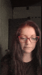 a young woman with long red hair and red glasses is looking at the camera .