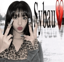 a woman making a peace sign in front of a sign that says sybau