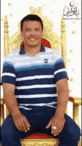 a man wearing a blue and white striped shirt is sitting on a gold chair