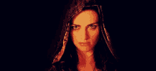 a woman wearing a hooded cloak is looking at the camera in a dark room .