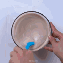 a person is mixing something in a bowl with a blue spoon and the words mr.cakes visible