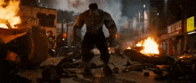 the hulk is standing in the middle of a city surrounded by fire .