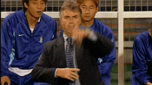 a man in a suit and tie is pointing while sitting in a soccer dugout