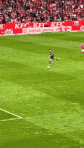 a soccer player is kicking a ball on a field with a kfc banner in the background