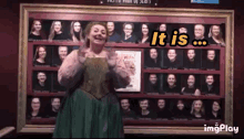 a woman in a green dress is standing in front of a wall of people with the words " it is " on it