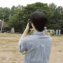 a man in a plaid shirt is taking a picture of a field with his cell phone .