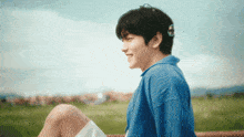 a young man in a blue shirt is sitting on a bench in a field