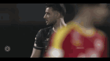 a soccer player in a black jersey is standing next to another player in a red shirt .