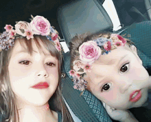 a little girl wearing a flower crown sits next to another little girl