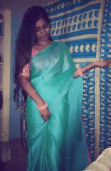 a woman in a green saree is standing in front of a blue and white curtain