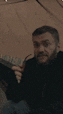 a man with a beard is sitting in a tent and holding a gun .