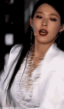 a close up of a woman wearing a white jacket and gold earrings .