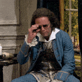 a man in a blue jacket adjusts his glasses